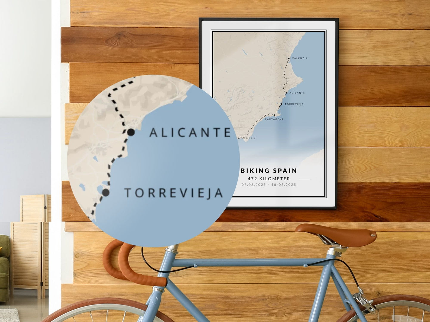 Reiseposter von einer Fahrradtour hängt an der Wand. Davor steht ein Fahrrad.